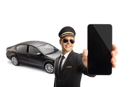 Professional chauffeur holding a smartphone in front of a black car isolated on white backgroundの写真素材