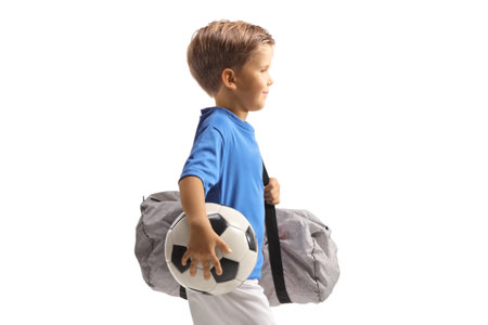 Profile shot of a boy wearing a sports jersey, holding a soccer ball and sports bag isolated on white backgroundの写真素材