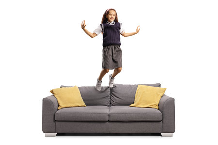 Schoolgirl in a uniform jumping on sofa isolated on white backgroundの写真素材