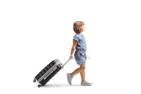 Full length profile shot of a little girl walking and pulling a suitcase isolated on white backgroundの写真素材