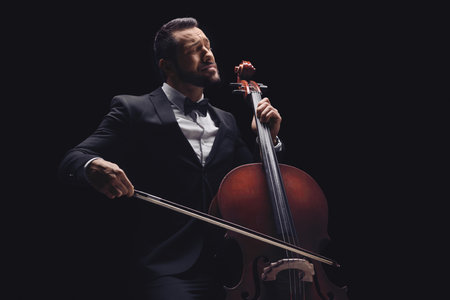 Male musician in a suit and bow-tie playing a cello over black background