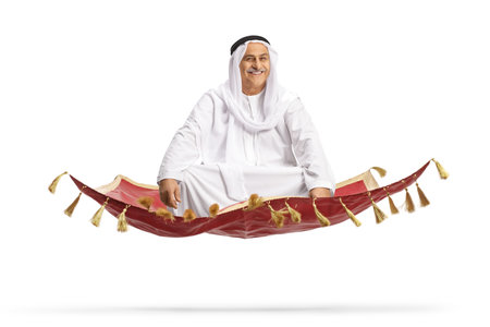 Mature arab man sitting on a carpet and flying isolated on white backgroundの写真素材