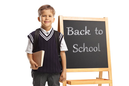 Schoolboy standing in front of a chalk board with text back to school isolated on white backgroundの写真素材