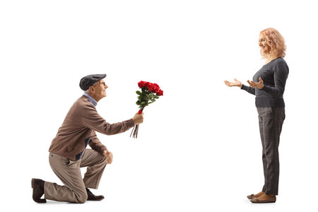 Senior man kneeling and giving a red roses to a woman isolated on white backgroundの写真素材