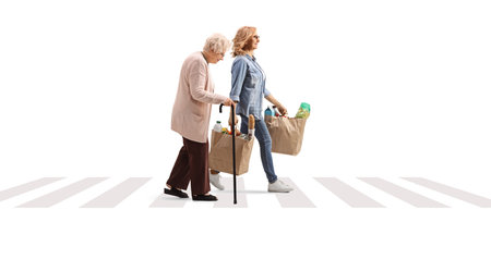 Woman with an elderly lady crossing street and carrying grocery bags isolated on white backgroundの写真素材