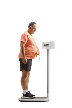 Mature man measuring waist and standing on a medical weight scale isolated on white backgroundの写真素材