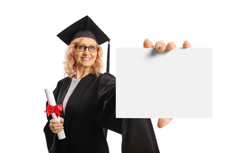 Mature woman in a graduation gown holding a diploma and showing blank card isolated on white backgroundの写真素材