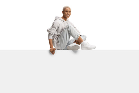 African american gen z guy with bleached hair sitting on a blank panel isolated on white backgroundの写真素材