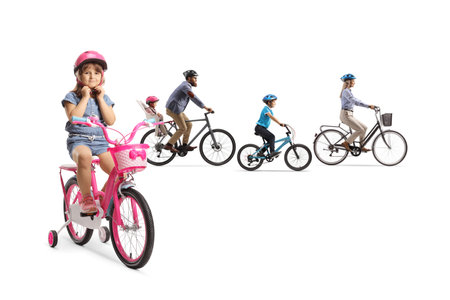 Family riding bicycles and a little girl with a bike putting on a helmet isolated on white backgroundの写真素材