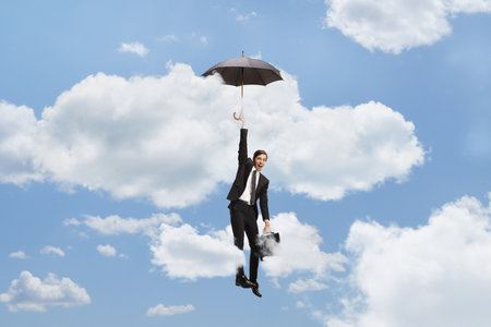 Businessman holding an umbrella and flying up in the skyの写真素材