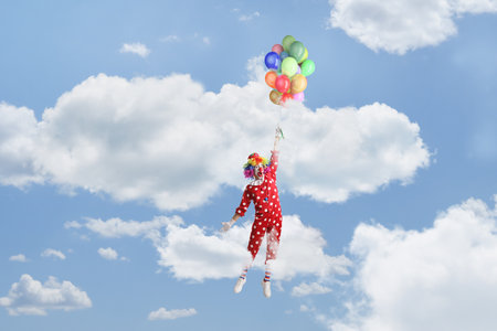 Funny clown holding a bunch of balloons and flying up in the skyの写真素材
