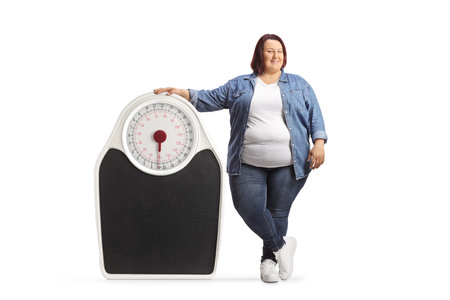 Overweight woman standing next to a medical scale and smiling isolated on white backgroundの写真素材