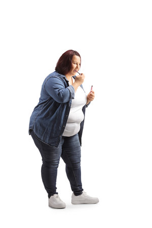 Overweight young woman in casual clothing standing and applying lip gloss isolated on white backgroundの写真素材
