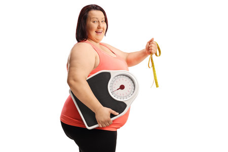 Cheerful overweight woman holding a tape and a weight scale isolated on white backgroundの写真素材