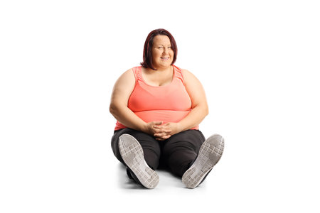 Overweight young woman in sportswear sitting on the ground isolated on white backgroundの写真素材
