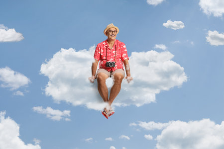 Happy mature male tourist with camera hanging around his neck sitting on a cloudの写真素材