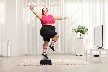 Cheerful overweight woman exercising step aerobics at home in front of a tvの写真素材
