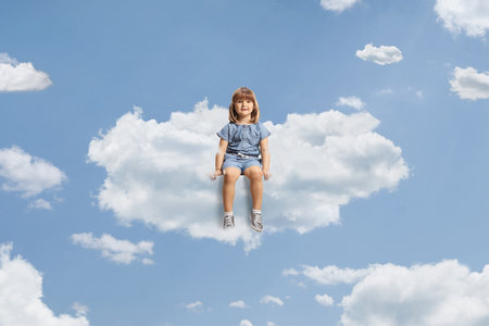 Little girl sitting on a cloud and smiling up in the skyの写真素材