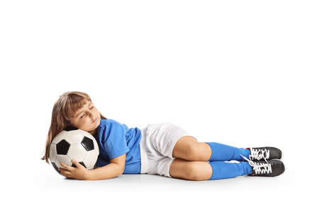 Little girl in a football kit sleeping with a ball isolated on white backgroundの写真素材