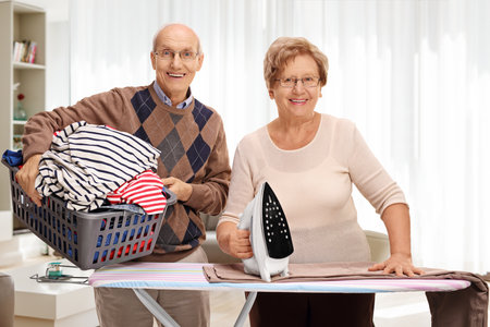 Cheerful senior couple ironing together in a living roomの写真素材