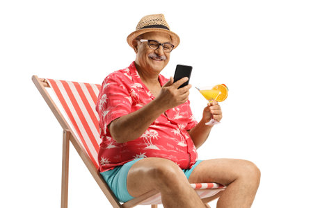 Mature male tourist sitting in a chair holding a cocktail and using a smartphone isolated on white backgroundの写真素材