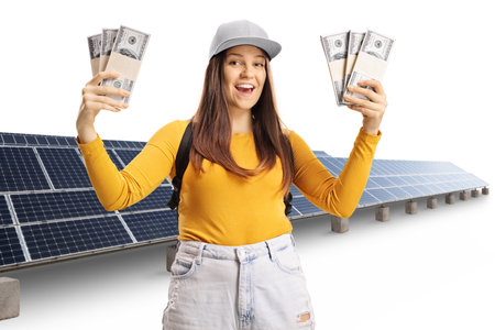 Young smiling female student holding stacks of money in front of photovoltaics isolated on white backgroundの写真素材