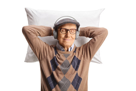 Elderly man with headphones resting on a pillow isolated on white backgroundの写真素材