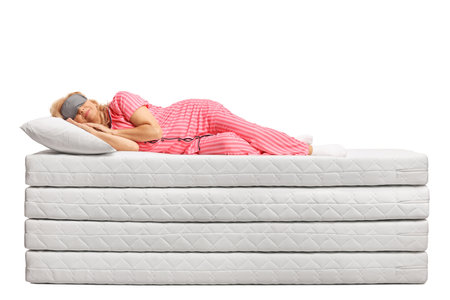 Woman in pajamas sleeping on a pile of mattresses isolated on white backgroundの写真素材