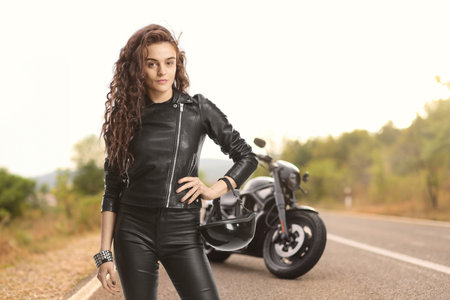 Woman in a leather jacket with a chopper posing on the roadの写真素材