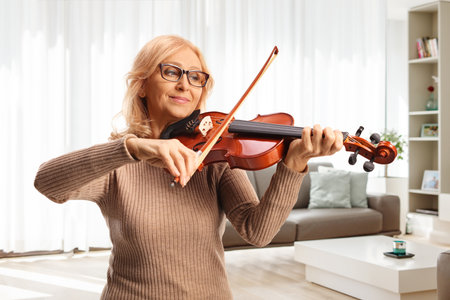Happy mature woman playing a violin at homeの写真素材