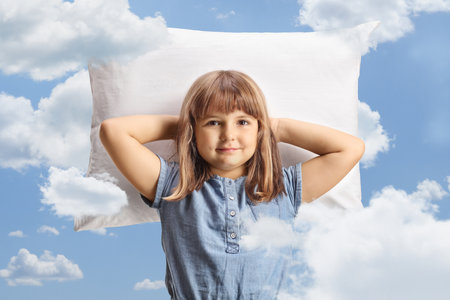 Cute little girl resting on a pillow among clouds on a blue skyの写真素材
