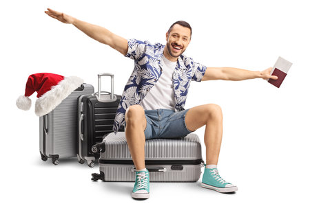 Happy male tourist going on a christmas trip, sitting on a suitcase and spreading arms to fly isolated on white backgroundの写真素材