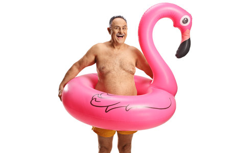 Happy mature man in swimming shorts with a big inflatable flamingo rubber ring isolated on white backgroundの写真素材