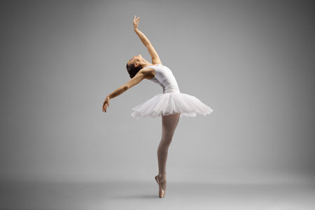 Full length shot of a ballerina dancing and leaning backwards isolated on gray backgroundの写真素材