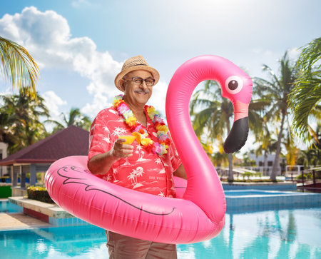 Mature male tourist with a flamingo rubber ring and a cocktail by the poolの写真素材