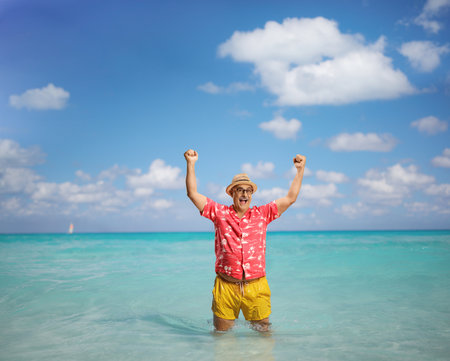 Overjoyed mature tourist on a summer holiday gesturing happiness with arms up in the seaの写真素材
