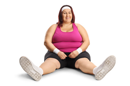 Smiling plus size woman in sportswear sitting on the ground isolated on white backgroundの写真素材