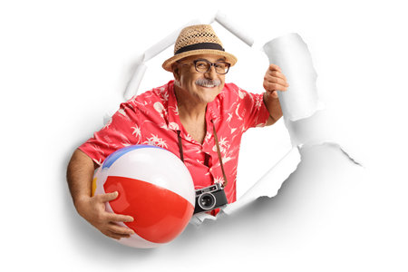 Mature male tourist peeking through a paper hole and holding a beach ball isolated on white backgroundの写真素材