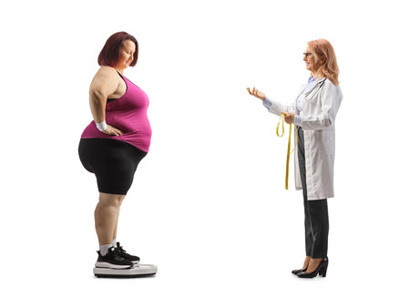 Full length profile shot of a female doctor talking to a corpulent woman in a weight scale isolated on white backgroundの写真素材