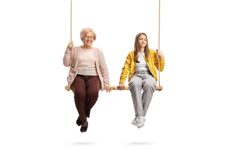 Grnadmother and teenage granddaughter sitting on a swing together isolated on white backgroundの写真素材