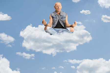 Bald man sitting corssed legged on a cloud and practicing meditation high up in the sky