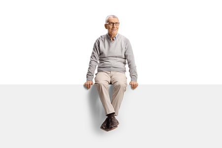 Cheerful elderly man sitting on a blank panel and smiling isolated on white backgroundの写真素材
