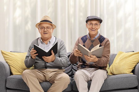 Elderly men sitting on a sofa and reading books in a living roomの写真素材
