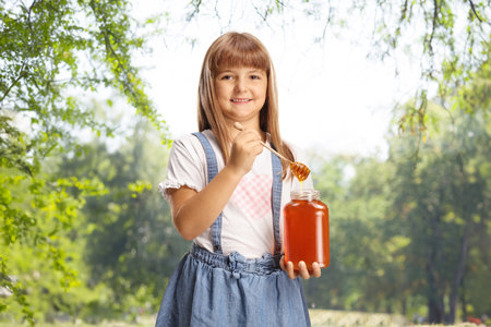 Little girl trying honey from a jar outdoors in natureの写真素材