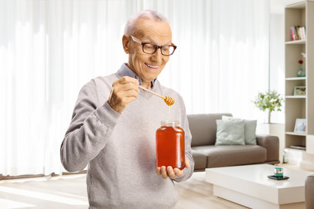 Elderly man holding a wooden dipper and a honey jar at homeの写真素材