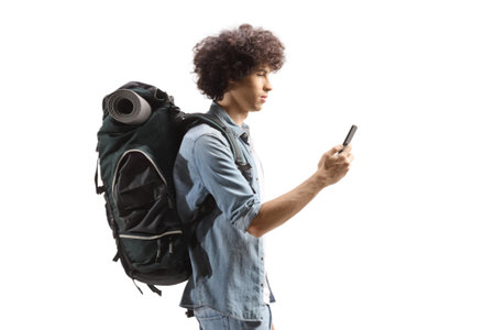 Profile shot of a young male backpacker walking and using a smartphone isolated on white backgroundの写真素材