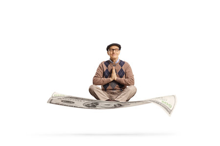 Elderly man sitting on a money banknote in a meditation pose isolated on white backgroundの写真素材