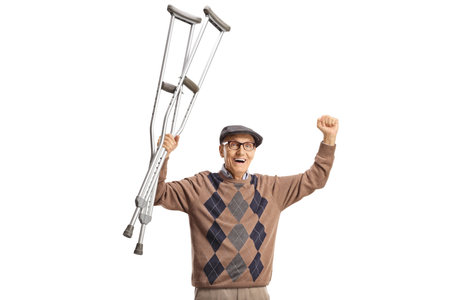 Happy elderly man holding crutches up isolated on white backgroundの写真素材