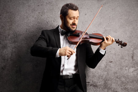 Elegant young man playing a violin and leaning on a gray wallの写真素材