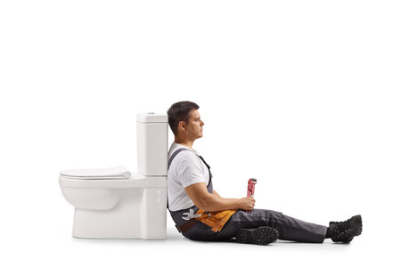 Tired plumber sitting next to a toilet isolated on white backgroundの写真素材